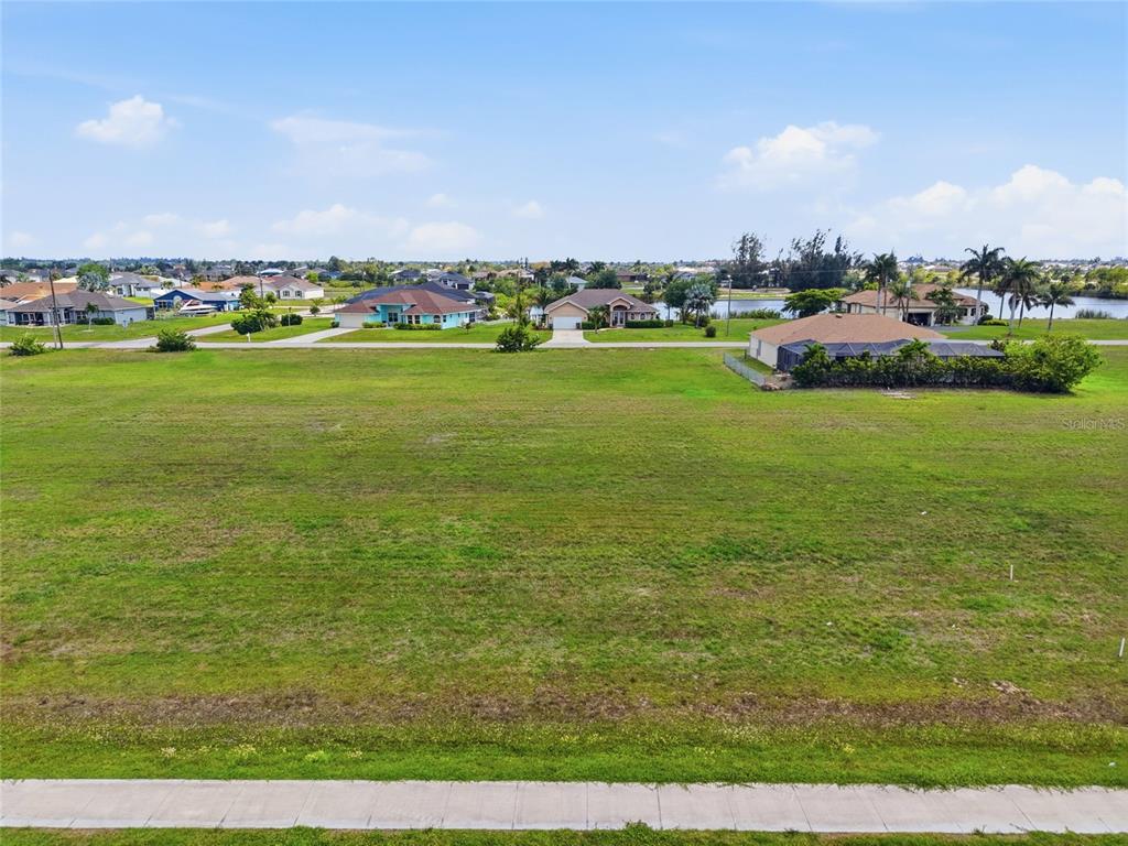 A large, vacant grassy lot sits in front of a residential neighborhood with a canal — 3008 TROPICANA PARKWAY W, CAPE CORAL, FL