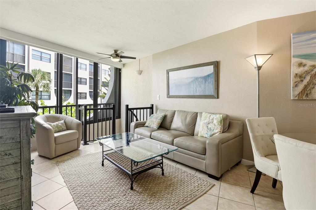 A living room features a beige sofa, glass coffee table, armchair, and large floor-to-ceiling windows — 1011 ANGLERS COVE UNIT H203, MARCO ISLAND, FL