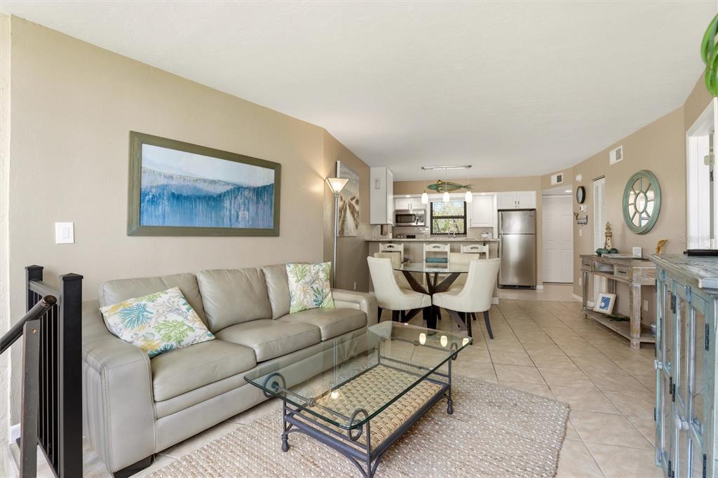 A living room with a leather sofa, glass coffee table, and an adjacent dining area — 1011 ANGLERS COVE UNIT H203, MARCO ISLAND, FL