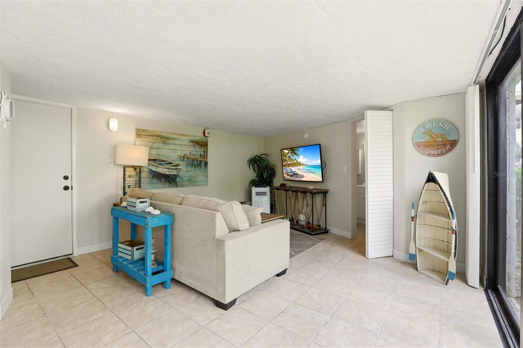 A living room with tile floors, a beige sofa, coastal decor, and a wall-mounted television — 1011 ANGLERS COVE UNIT H203, MARCO ISLAND, FL