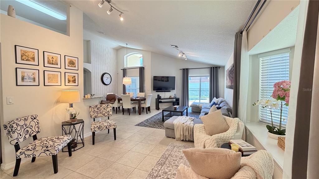 This open-concept living and dining area features tile flooring, vaulted ceilings, and neutral decor — 2513 DHARMA CIRCLE, KISSIMMEE, FL
