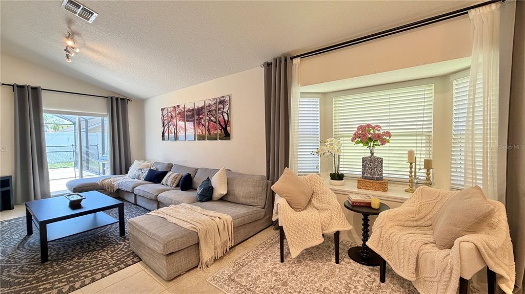 A living room features a gray sectional sofa, two armchairs, and a large bay window — 2513 DHARMA CIRCLE, KISSIMMEE, FL