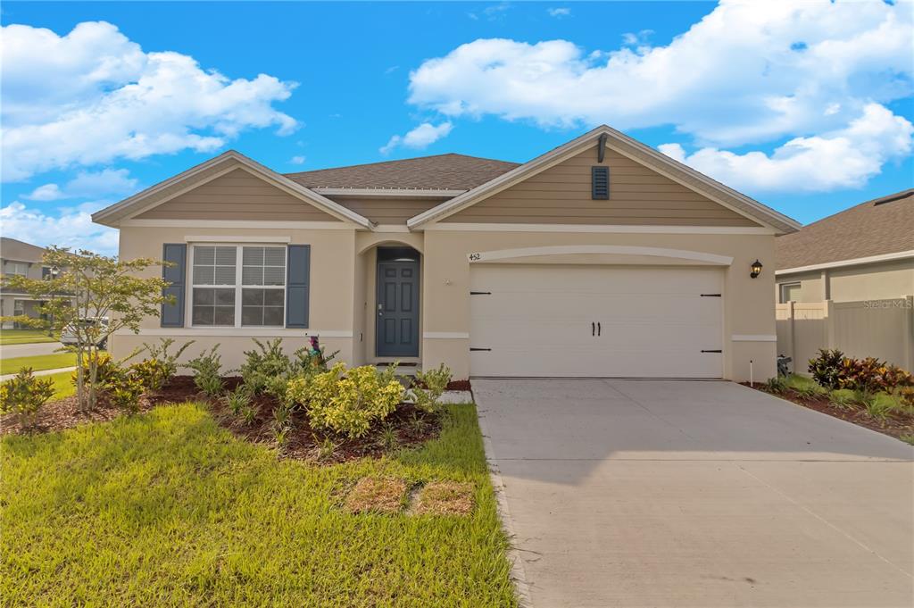 A single-story suburban house with a tan stucco exterior, a two-car garage, and blue shutters — 452 NOBLE AVENUE, DAVENPORT, FL