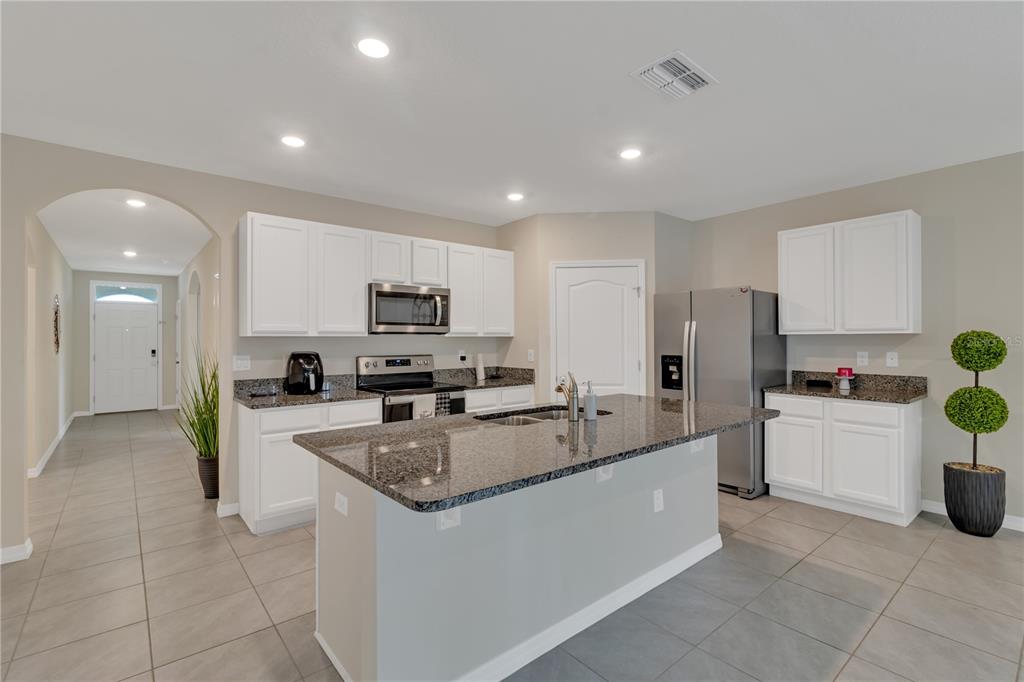 A kitchen features white cabinets, granite countertops, a center island, and stainless steel appliances — 452 NOBLE AVENUE, DAVENPORT, FL