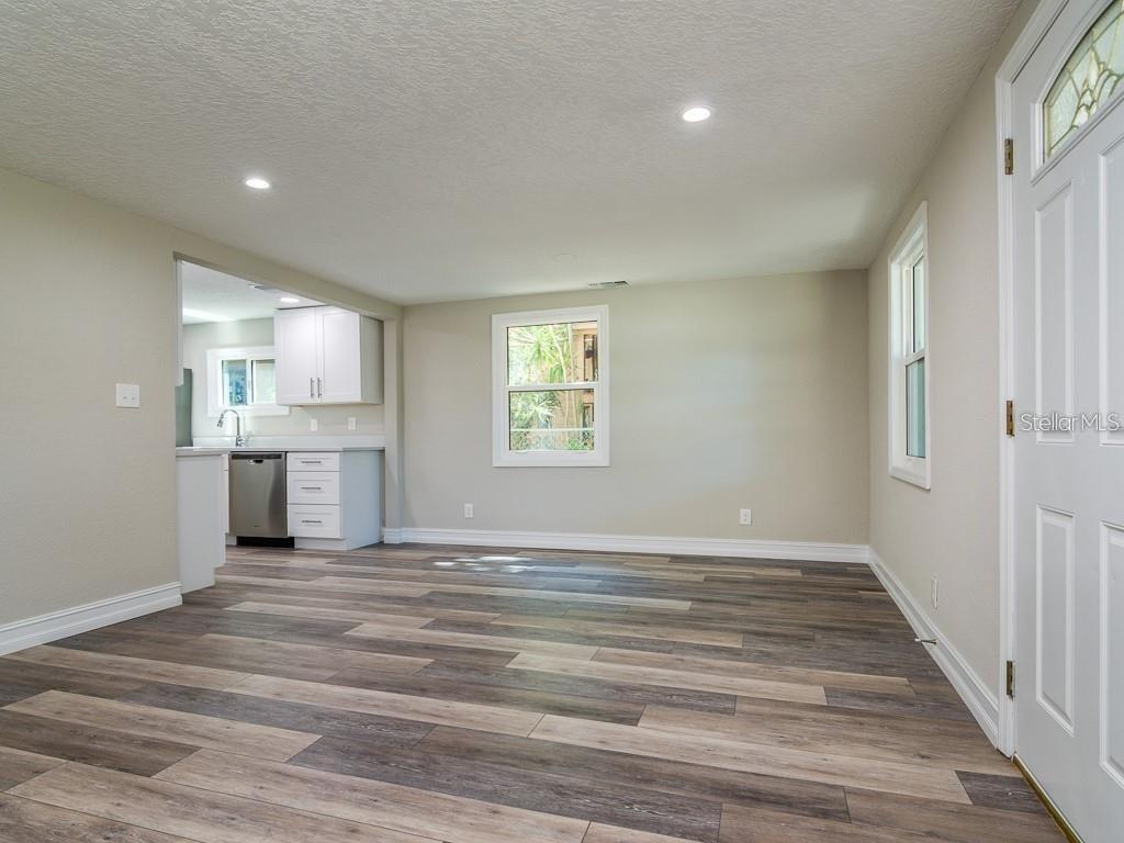 An open-concept dining area with wood-look flooring leads into a kitchen with white cabinets — 7225 33RD STREET N, ST PETERSBURG, FL