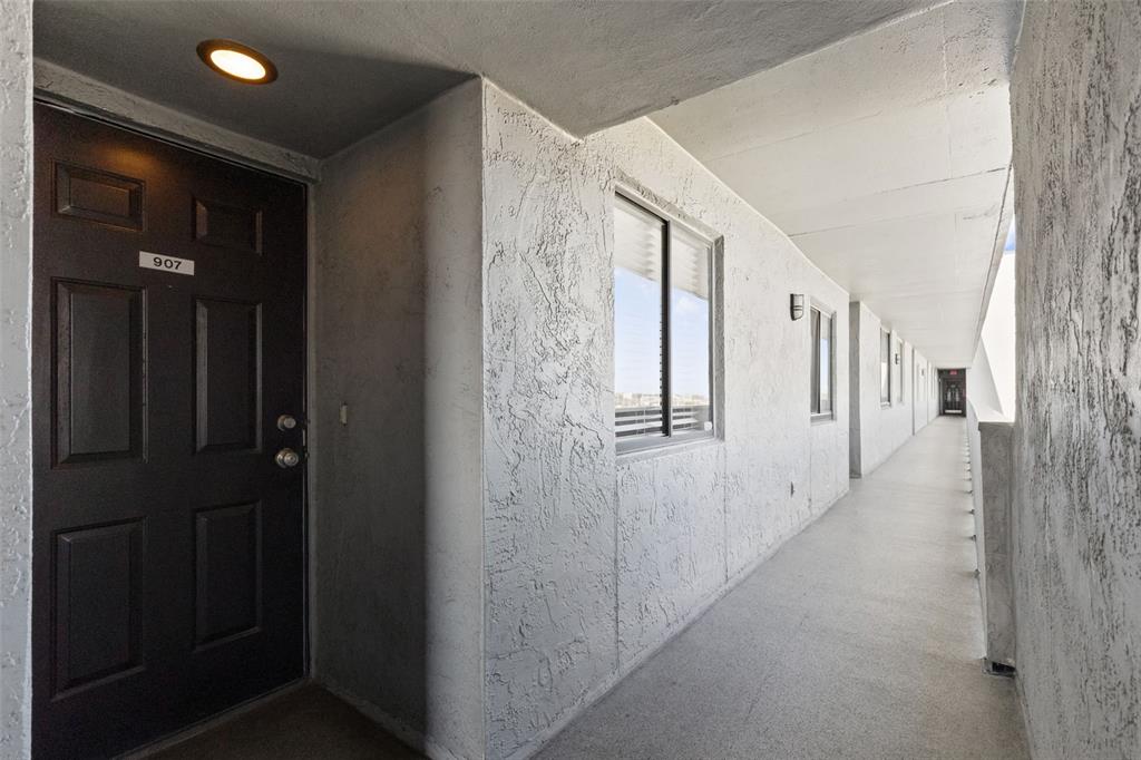 An exterior apartment hallway features a dark door numbered 907 and textured white walls — 201 W LAUREL STREET UNIT 907, TAMPA, FL