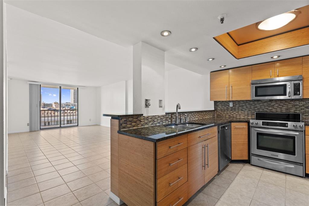 A kitchen with wood cabinets and granite countertops overlooks an open living area with tile floors — 201 W LAUREL STREET UNIT 907, TAMPA, FL