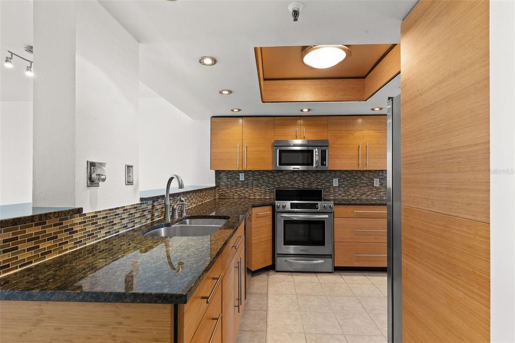 A kitchen features light wood cabinets, dark granite countertops, stainless steel appliances, and tile flooring — 201 W LAUREL STREET UNIT 907, TAMPA, FL