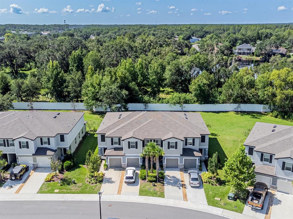 An aerial view shows three multi-story townhomes with attached garages and a white privacy fence — 21372 DARTER ROAD, LAND O LAKES, FL