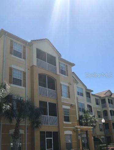 A multi-story apartment building features tan stucco walls, screened balconies, and a palm tree — 3314 ROBERT TRENT JONES DRIVE UNIT 406, ORLANDO, FL