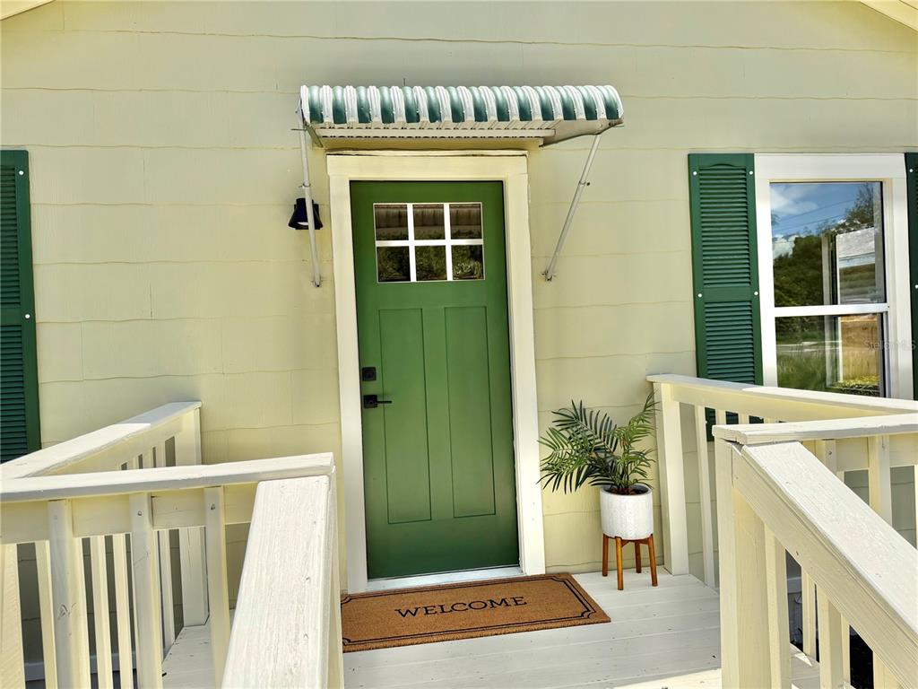 A green front door with a small awning sits on a porch with a welcome mat — 3530 51ST AVENUE N, ST PETERSBURG, FL