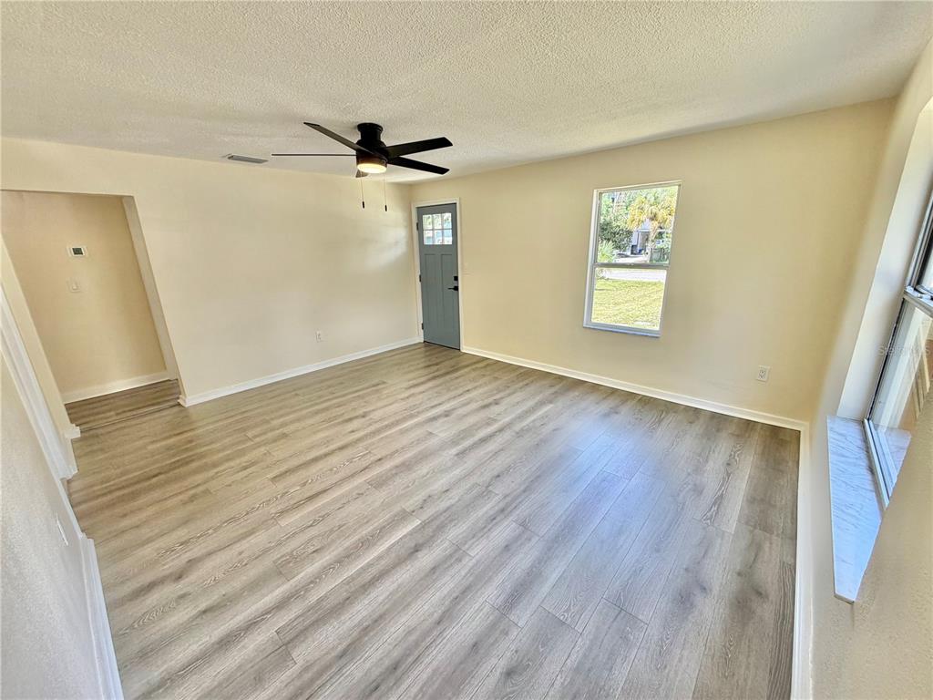 An empty room features light wood-look flooring, a ceiling fan, and a blue exterior door — 3530 51ST AVENUE N, ST PETERSBURG, FL