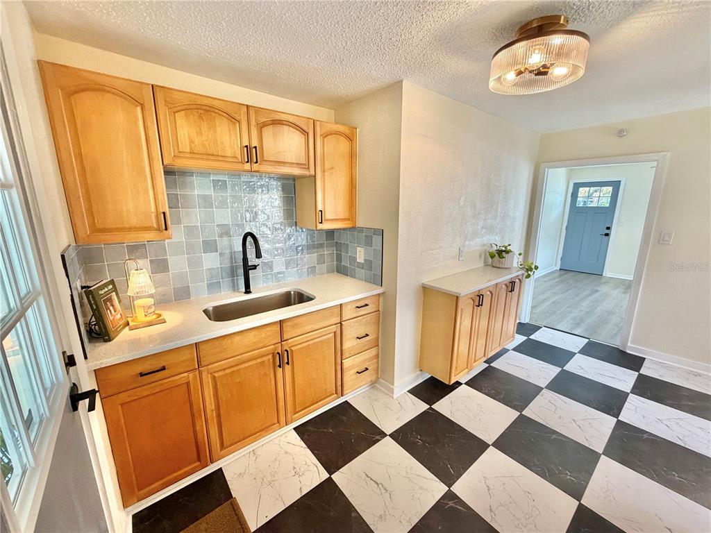 A kitchen features light wood cabinets, a black faucet, gray tile backsplash, and checkered flooring — 3530 51ST AVENUE N, ST PETERSBURG, FL