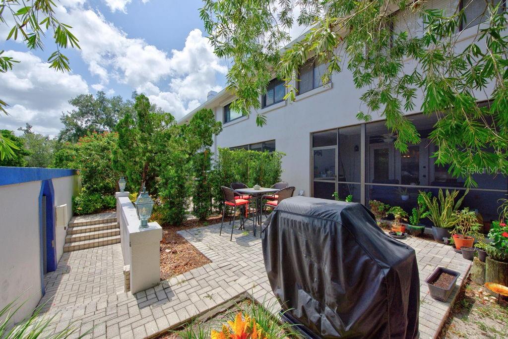 A paved patio features a dining set, a covered grill, and stairs leading to a wall — 1672 WATERMARK CIRCLE NE, ST PETERSBURG, FL