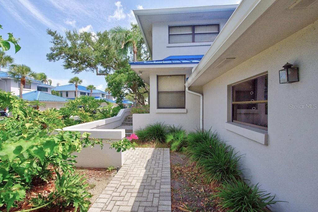 A paved walkway leads to the side entrance of a two-story home with blue roofs — 1672 WATERMARK CIRCLE NE, ST PETERSBURG, FL