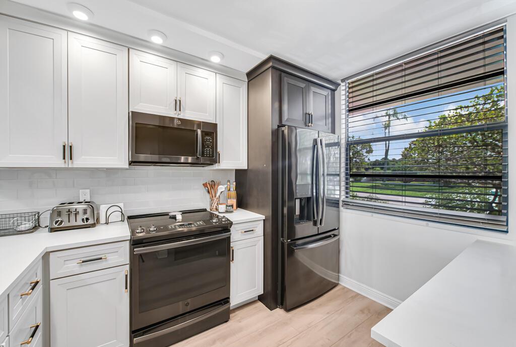 A kitchen features white cabinets, a black stove and refrigerator, and a window with blinds — 3710 Whitehall Drive # 105, West Palm Beach FL 33401, WEST PALM BEACH, FL