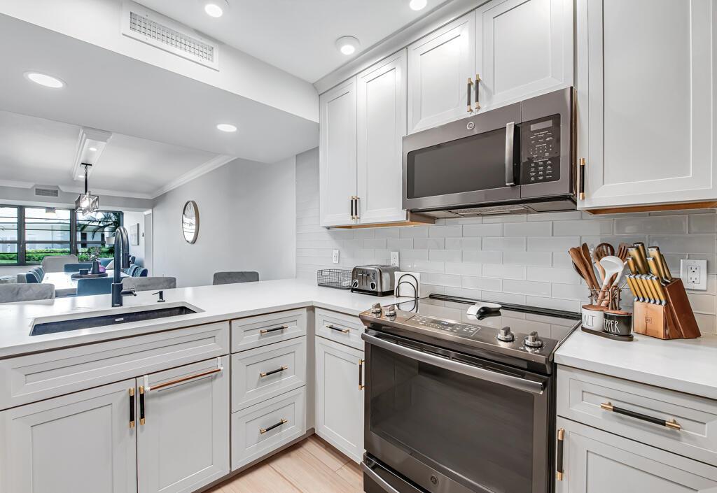 A kitchen featuring white cabinets, stainless steel appliances, a subway tile backsplash, and quartz countertops — 3710 Whitehall Drive # 105, West Palm Beach FL 33401, WEST PALM BEACH, FL