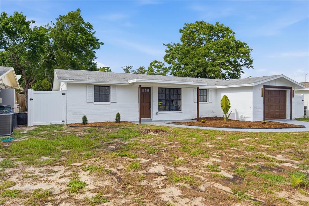 A single-story white house with a brown front door, garage, and a patchy grass yard — 7811 TYSON DRIVE, PORT RICHEY, FL