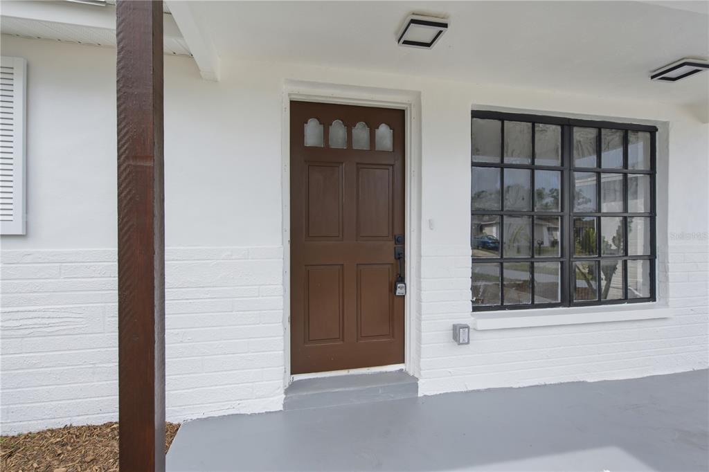 A brown front door with glass panes sits beside a large window on a porch — 7811 TYSON DRIVE, PORT RICHEY, FL