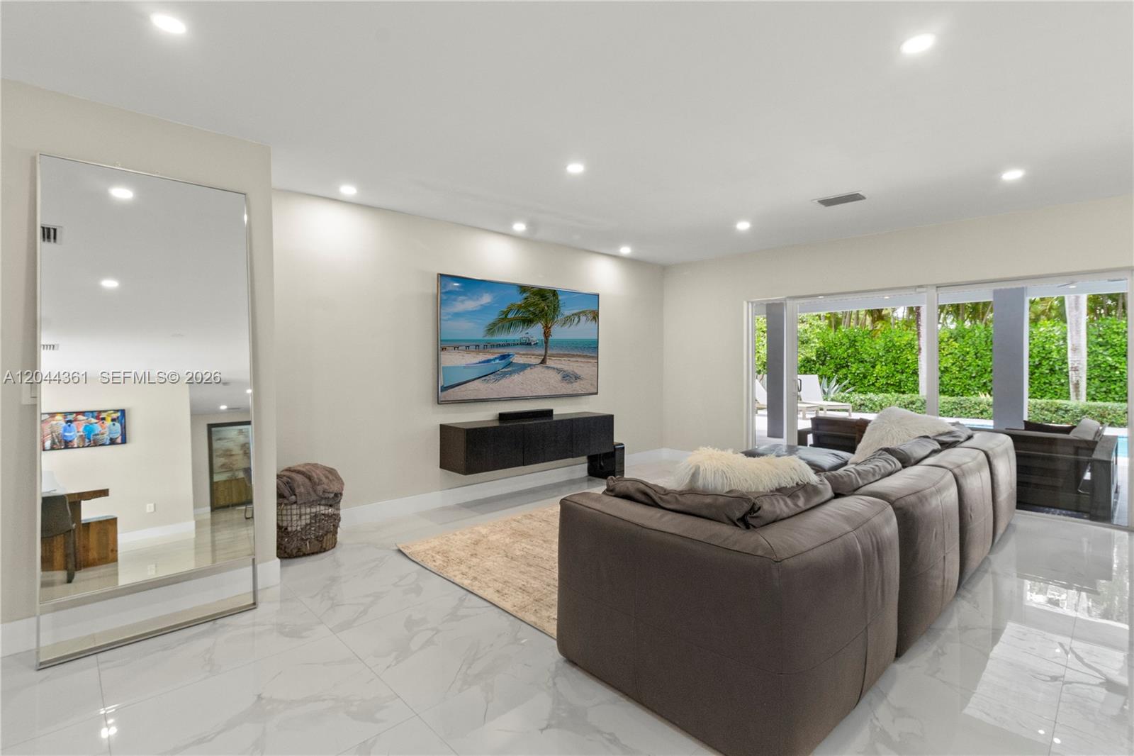 A modern living room features a large sectional sofa, wall-mounted television, and floor-to-ceiling mirror — 12900 SW 112th Ave, Miami FL 33176, MIAMI, FL