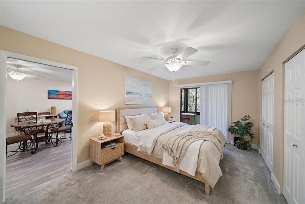 A bedroom with a queen bed, beige walls, carpeted flooring, and an adjacent dining area — 257 SHERWOOD DRIVE UNIT 257, BRADENTON, FL