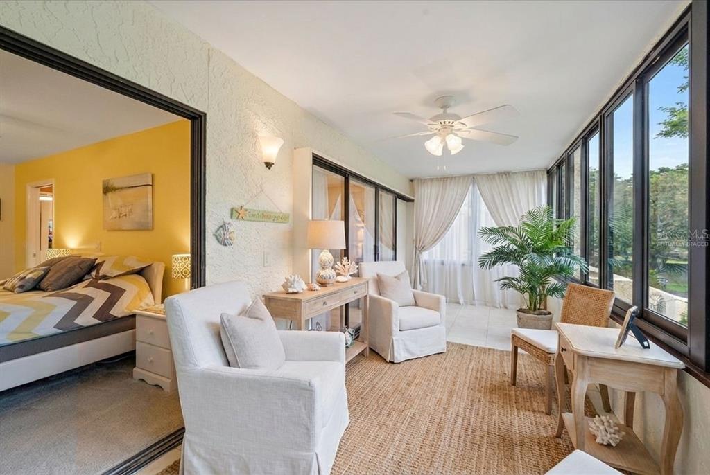 A sunroom with white armchairs, a jute rug, and large windows overlooks a green area — 257 SHERWOOD DRIVE UNIT 257, BRADENTON, FL