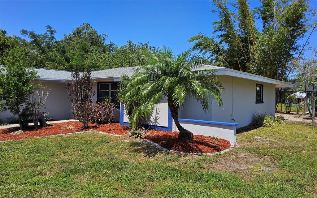 A single-story house with a palm tree, red mulch landscaping, and blue trim accents — 1108 AMPLE AVENUE, PORT CHARLOTTE, FL
