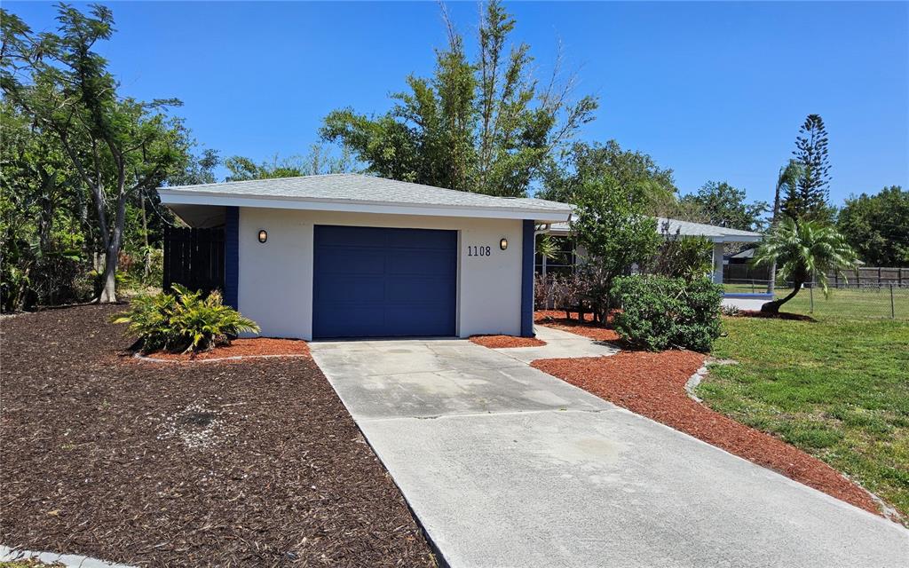 A single-story house with a blue garage door, a concrete driveway, and surrounding landscaping — 1108 AMPLE AVENUE, PORT CHARLOTTE, FL