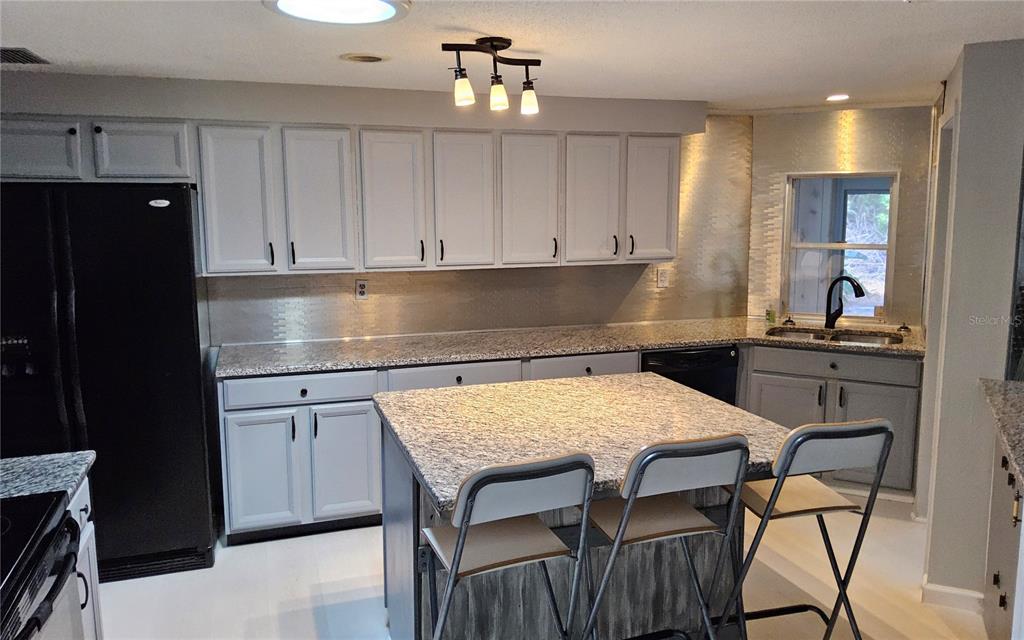 A kitchen features light gray cabinets, granite countertops, a central island, and a black refrigerator — 1108 AMPLE AVENUE, PORT CHARLOTTE, FL