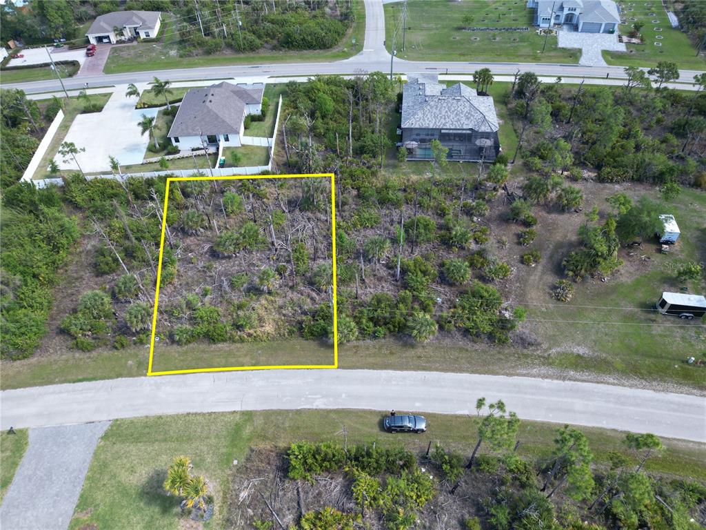An aerial view shows a vacant, wooded residential lot outlined in yellow along a road — 14390 DAFOE STREET, PORT CHARLOTTE, FL