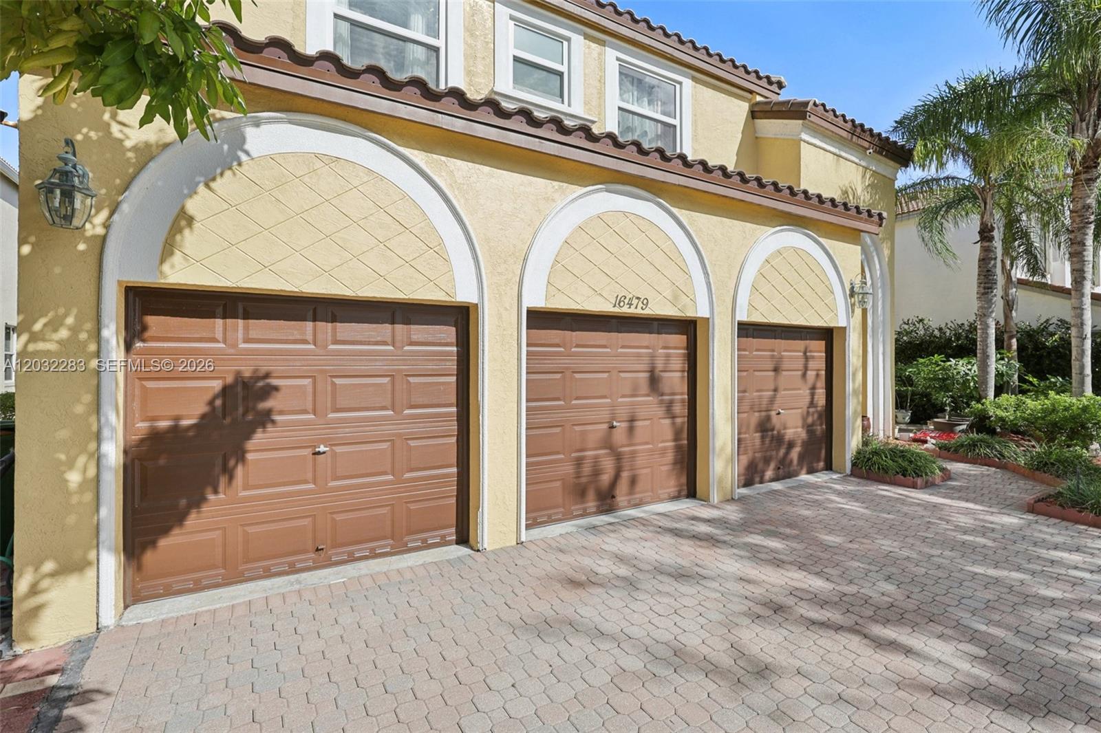 A three-car garage with brown doors and arched decorative stucco accents on a paved driveway — 16479 SW 54th Ct, Miramar FL 33027, MIRAMAR, FL