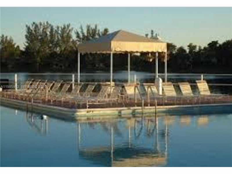 A swimming pool with lounge chairs and a shaded canopy sits beside a lake — 3720 INVERRARY DR # 2M, Lauderhill FL 33319, LAUDERHILL, FL