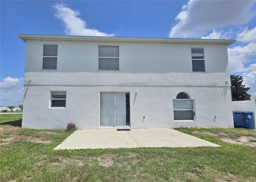 The rear exterior of a two-story white stucco house features a concrete patio and windows — 145 VISTA VIEW AVENUE, EAGLE LAKE, FL