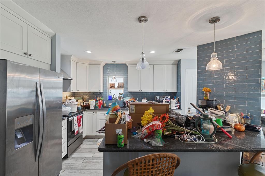 A kitchen with white cabinets, blue tiled walls, stainless steel appliances, and a dark island — 6645 FREEPORT DRIVE, SPRING HILL, FL