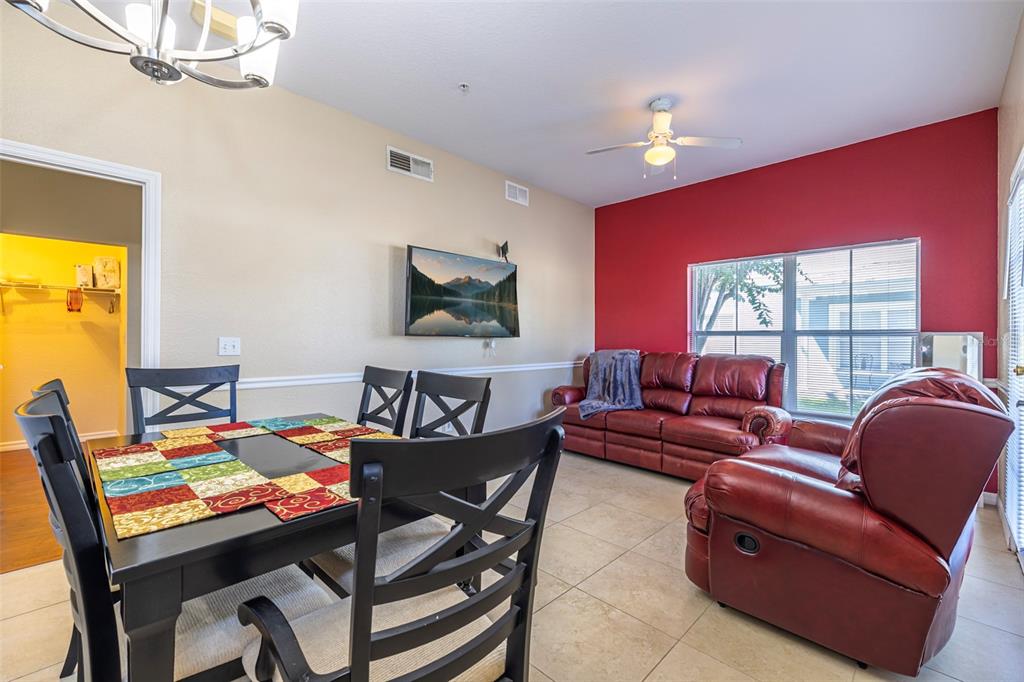 A dining area with a dark table and chairs opens into a living room space — 2208 SAN VITTORINO CIRCLE UNIT 107, KISSIMMEE, FL