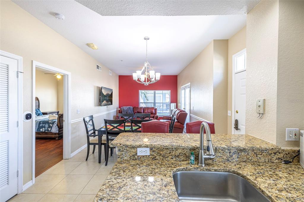 A kitchen sink with granite countertops overlooks a dining area and living room with red walls — 2208 SAN VITTORINO CIRCLE UNIT 107, KISSIMMEE, FL