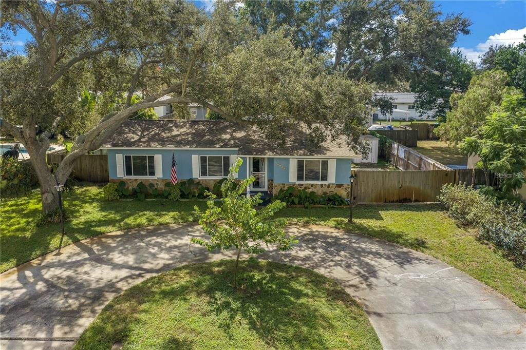 An exterior view of a blue single-story house with a circular driveway and large trees — 6144 2ND AVENUE N, ST PETERSBURG, FL