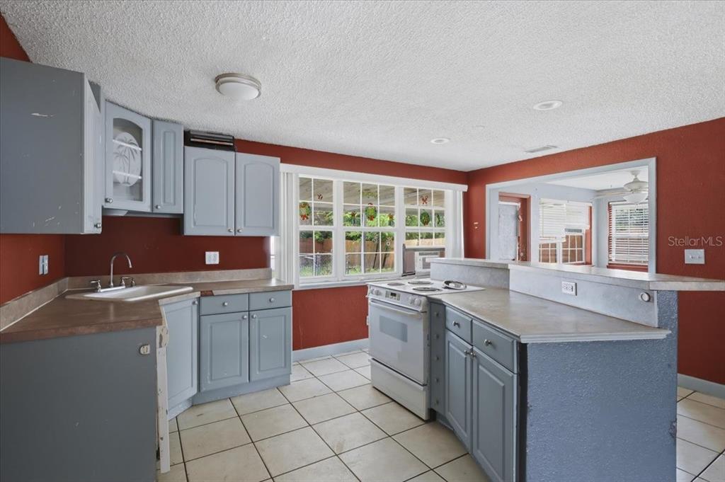 A kitchen with blue cabinets, red walls, white tile floors, and a white stove — 2605 YALE ROAD, SOUTH DAYTONA, FL