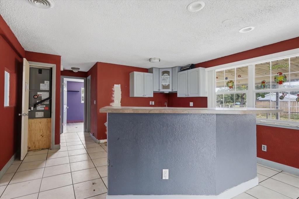 A kitchen with a gray breakfast bar, red walls, light-colored cabinets, and tile flooring — 2605 YALE ROAD, SOUTH DAYTONA, FL