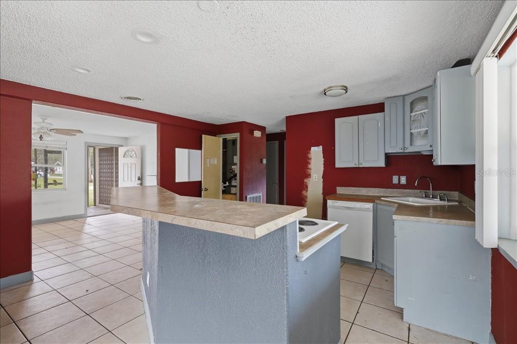 A kitchen with a breakfast bar, gray cabinets, and red walls opens to a living area — 2605 YALE ROAD, SOUTH DAYTONA, FL
