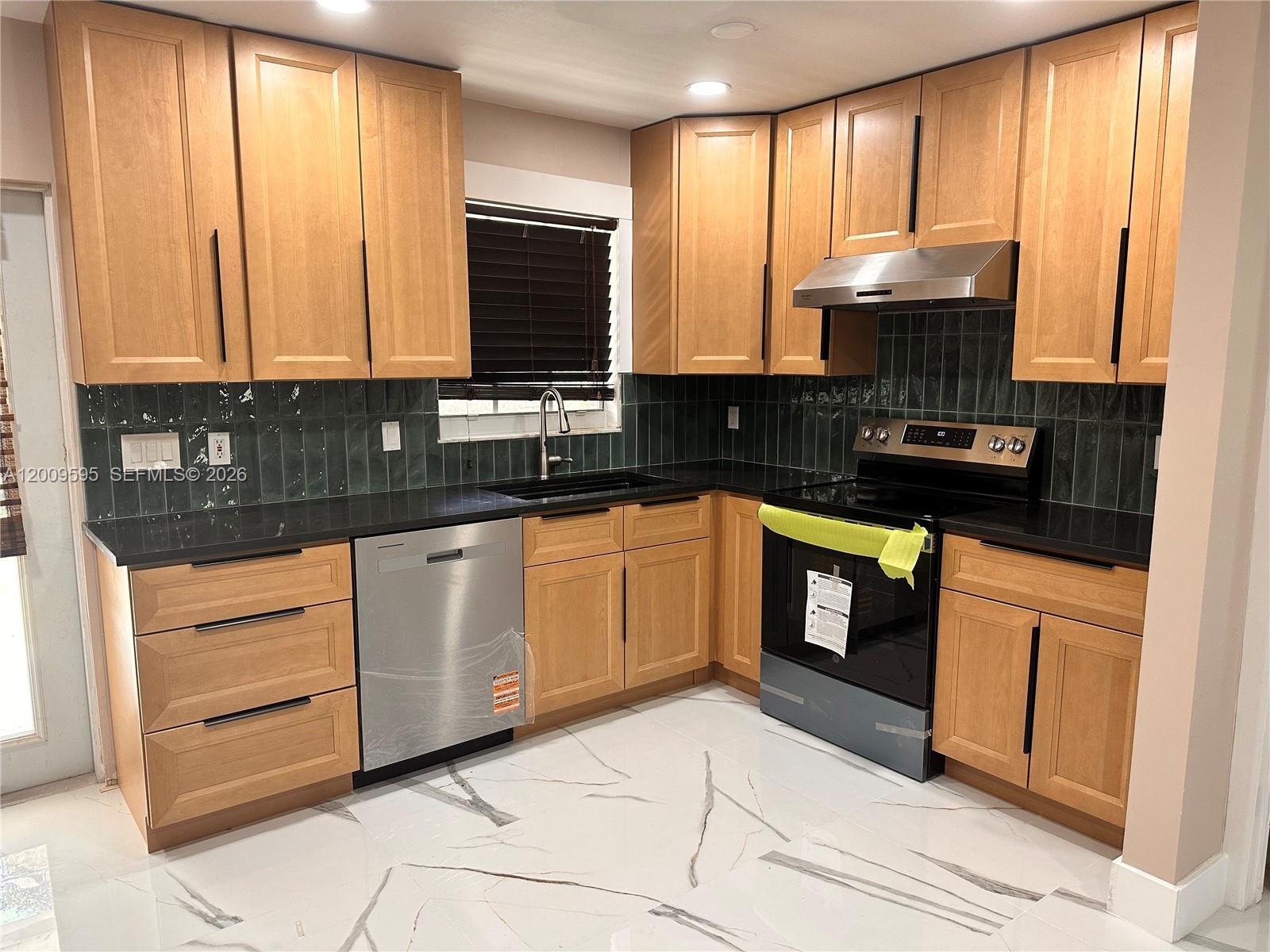 A kitchen features light wood cabinets, black countertops, dark green tile backsplash, and marble-patterned flooring — 3614 Everglades Rd, Palm Beach Gardens FL 33410, PALM BEACH GARDENS, FL