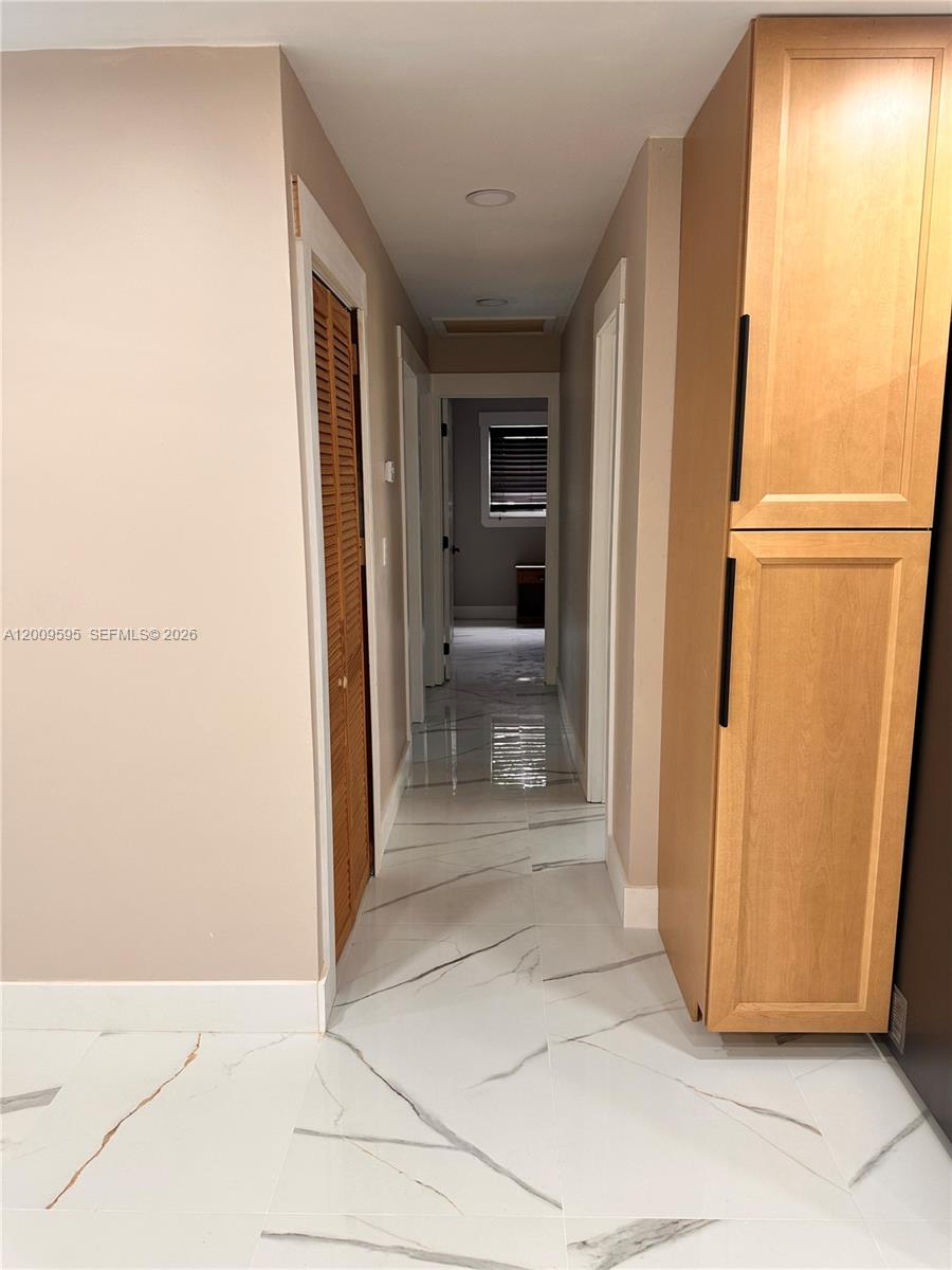 A narrow hallway features white marble-look tile flooring, light-colored walls, and a tall wooden cabinet — 3614 Everglades Rd, Palm Beach Gardens FL 33410, PALM BEACH GARDENS, FL