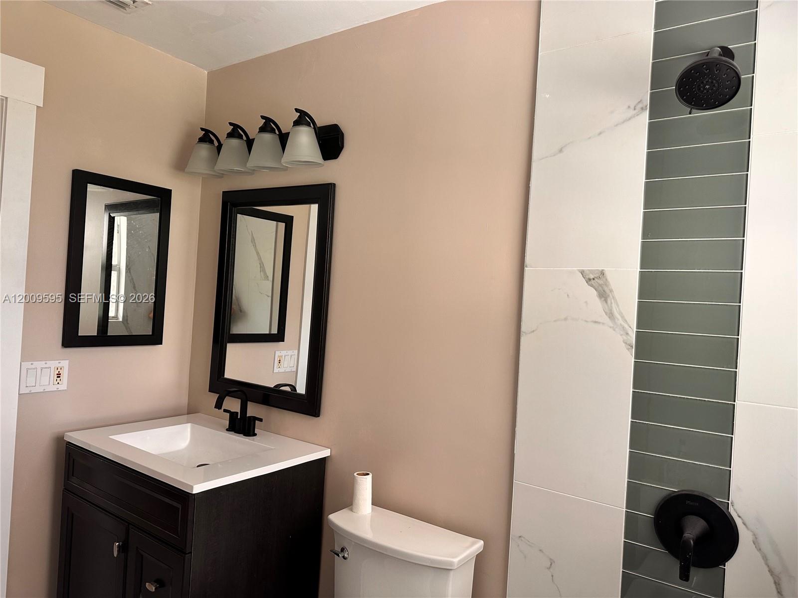A bathroom features a dark vanity, black-framed mirrors, and a shower with marble-look and green tiles — 3614 Everglades Rd, Palm Beach Gardens FL 33410, PALM BEACH GARDENS, FL