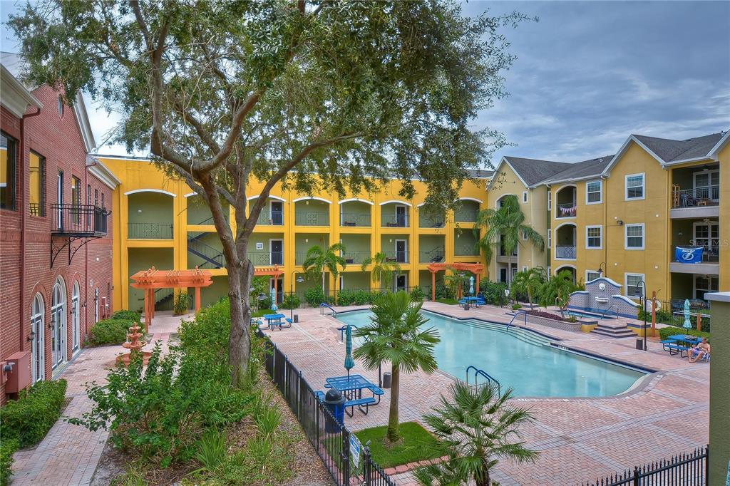 An outdoor swimming pool area surrounded by yellow and brick apartment buildings with palm trees — 1910 E PALM AVENUE UNIT 11117, TAMPA, FL