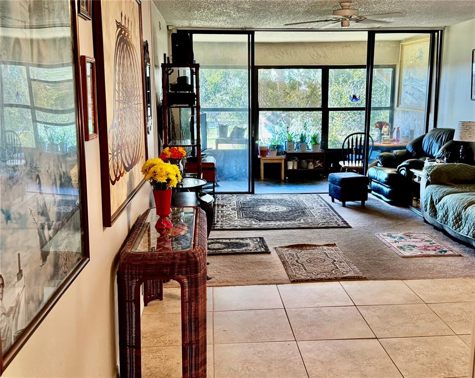 A living room features tile flooring, a wicker console table, and a glass-enclosed sunroom beyond — 12300 VONN ROAD UNIT 5304, LARGO, FL