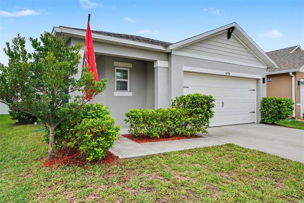 A single-story house with a gray stucco exterior, a white garage door, and landscaping — 6784 HUNTLEIGH HAMMOCK ROAD, ST CLOUD, FL