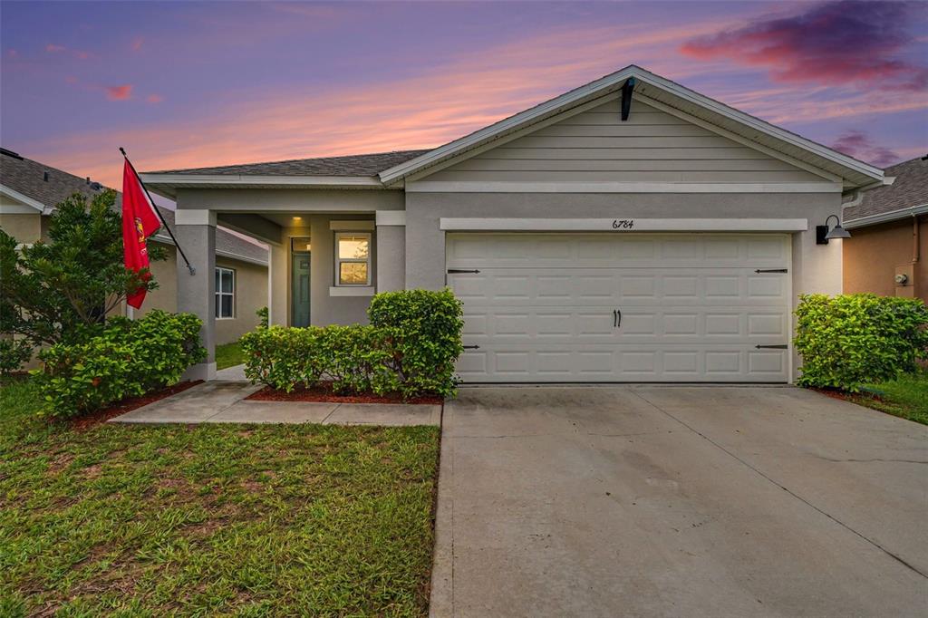A single-story house with a gray stucco exterior, a two-car garage, and a front lawn — 6784 HUNTLEIGH HAMMOCK ROAD, ST CLOUD, FL