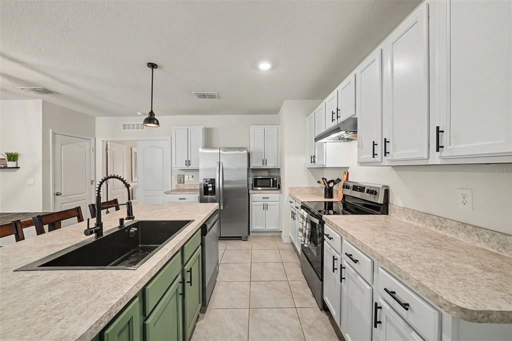 A kitchen features white upper cabinets, green lower island cabinets, stainless steel appliances, and countertops — 6784 HUNTLEIGH HAMMOCK ROAD, ST CLOUD, FL
