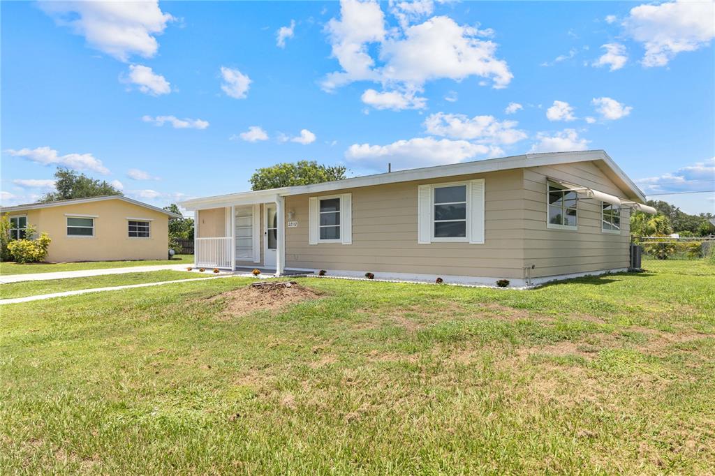 A tan, single-story house with a white porch and a large grassy front yard — 22312 LASALLE ROAD, PORT CHARLOTTE, FL