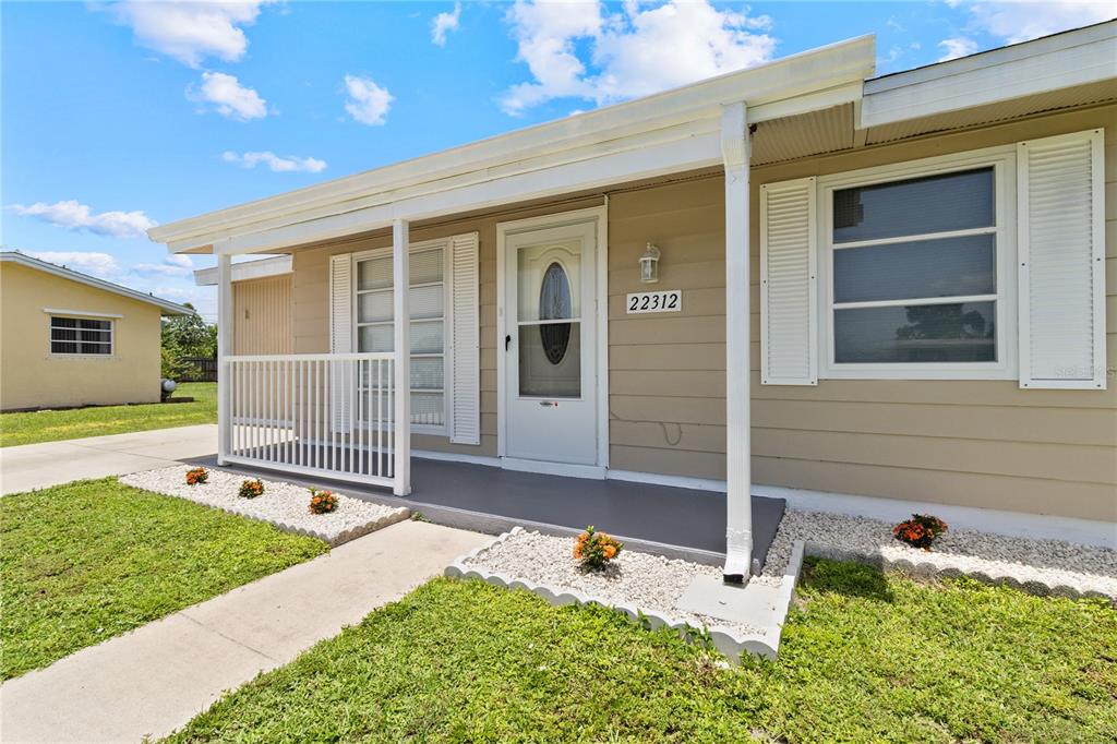 A tan house with a white porch railing, front door, and gravel landscaping beds — 22312 LASALLE ROAD, PORT CHARLOTTE, FL
